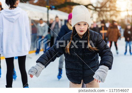Portrait of little kid girl friend enjoy having fun at outdoor ice skating rink while travel in old european city in winter cold sunny day. Children holiday sport activities 117354607