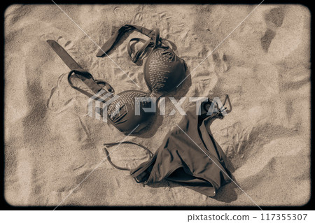 A black bikini is resting on warm sand under the sun 117355307