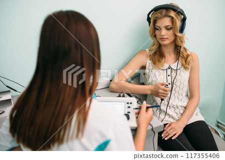 Woman undergoing hearing test while seated with clinician in a light-colored room, focusing on results during a bright daytime Woman undergoing hearing test while seated with clinician in a light-colored room, focusing on results during a bright daytime 117355406