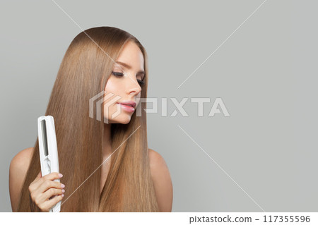 Lovely fashion model woman using hair straighteners iron on white background.  117355596