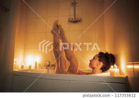 A woman is in a bathtub with candles lit around her. She is barefoot and has her legs up in the air. A woman is in a bathtub with candles lit around her. She is barefoot and has her legs up in the air. 117355612