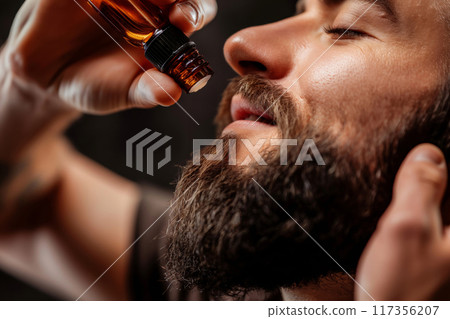 Close-up capture of a man using dropper bottle to massage beard oil into his facial hair 117356207