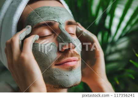 Relaxed male with a natural clay face mask for a pampering skincare treatment 117356241