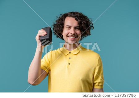 Young curly haired man listening music, wireless portable speaker - sound system Young curly haired man listening music, wireless portable speaker - sound system 117357790