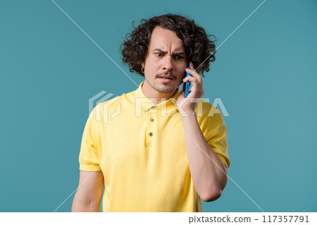 Irritated handsome man talking on mobile phone. Guy in stress, Blue studio. 117357791