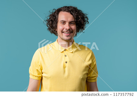Friendly man smiling portrait. Positive curly guy in yellow polo on blue studio Friendly man smiling portrait. Positive curly guy in yellow polo on blue studio 117357792