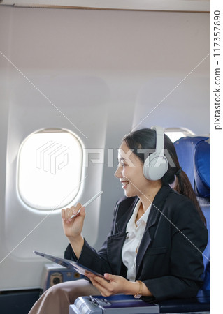 A woman wearing headphones and a black jacket is sitting on an airplane 117357890