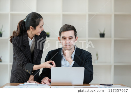 A woman and a man are sitting at a desk with a laptop in front of them 117357937