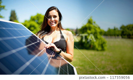 Smiling Woman Examining Solar Panel in Sunny Park 117359056