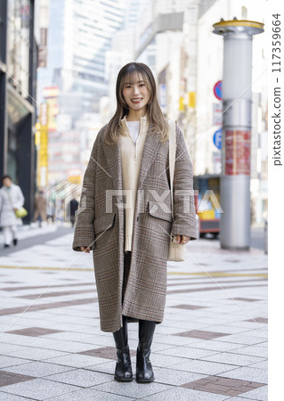 A woman in her 20s wearing a long coat and smiling at the camera, full body portrait 117359664