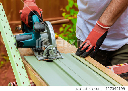 Worker cut plastic vinyl siding to size using circular handsaw before installing it Worker cut plastic vinyl siding to size using circular handsaw before installing it 117360199