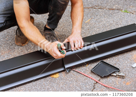 An aluminum rain gutter is bent using machine tool then cut to the required dimensions with shears 117360208
