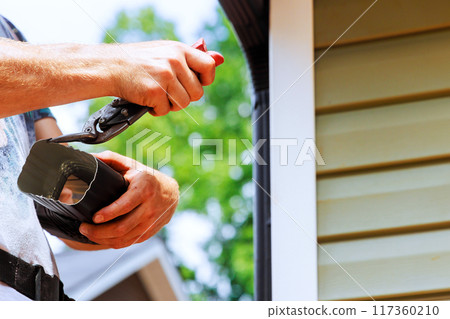 Preparation aluminum rain gutters before of cutting by worker using metal shears 117360210