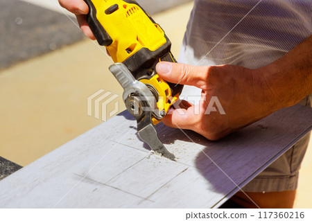 With help of multitool, worker is making hole in laminate panel for outlet 117360216