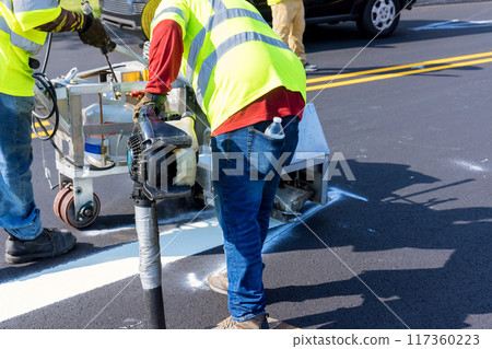 Workers use an airbrush machine to apply markings to road after asphalt has been laid Workers use an airbrush machine to apply markings to road after asphalt has been laid 117360223