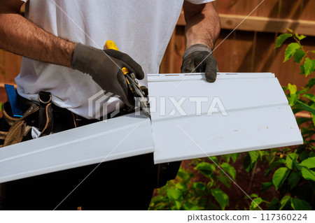 Worker cuts plastic vinyl siding to size before it is installed using scissors Worker cuts plastic vinyl siding to size before it is installed using scissors 117360224