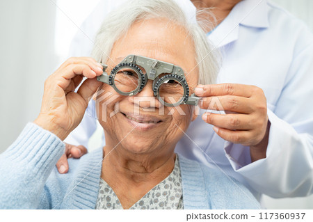 Optometrist checking Asian elderly woman ophthalmic vision eye test and using optical trial frame. 117360937