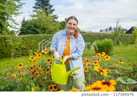 Happy woman taking care of flowers outdoors in garden, watering with can. Female preparing for preparing flowers for international women day. High quality photo 117360976