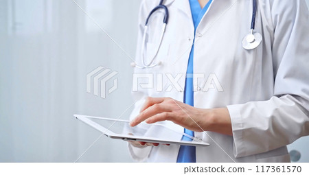 Doctor woman is using digital tablet in clinic. Healthcare professional with a stethoscope operating a touch screen tablet computer while standing straight. Medicine concept Doctor woman is using digital tablet in clinic. Healthcare professional with a stethoscope operating a touch screen tablet computer while standing straight. Medicine concept 117361570