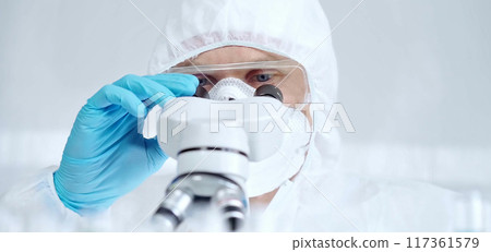Professional scientist in protective gear is using microscope in a laboratory setting, close-up of researcher. Science and medicine concepts Professional scientist in protective gear is using microscope in a laboratory setting, close-up of researcher. Science and medicine concepts 117361579