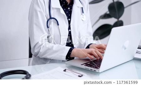 Doctor woman is typing on laptop computer at glass table in clinic. Medicine and pharmacy concept 117361599