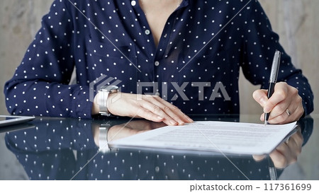 Businesswoman is signing corporate contract at her office desk in formal dark blue blouse with polka dots. Business people concept 117361699