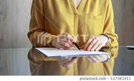 Businesswoman in yellow blues analyzing document at desk. Close-up of a professional auditor or lawyer reviewing a lengthy paper report in office setting. Business people concept 117361911