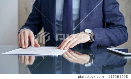 Businessman reviewing documents at office desk. Close-up of a professional man's hands examining paperwork with pen and tablet in sight. Business people concept 117361938