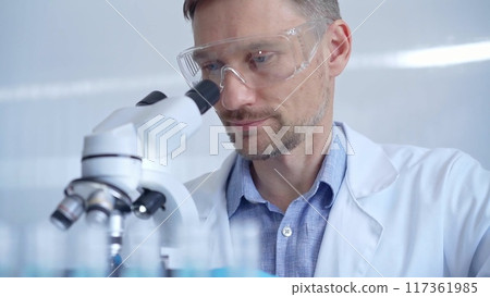 Man scientist with protective glasses and gloves is using microscope in laboratory, portrait of researcher. Microbiology science concept Man scientist with protective glasses and gloves is using microscope in laboratory, portrait of researcher. Microbiology science concept 117361985