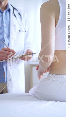 Doctor and patient. Physician is making notes on a clipboard while patient woman is describing something. Pediatrician, medicine concept 117362166