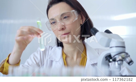 Scientist researcher with protective glasses examining lab tube Scientist researcher with protective glasses examining lab tube 117362182