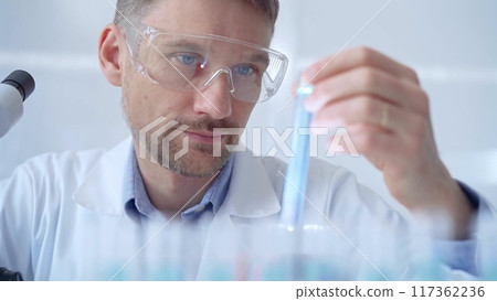 Scientist researcher with protective glasses examining lab tube 117362236