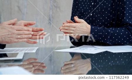 Unrecognizable business people shaking hands and clapping over glass table after contract signing in office. Agreement and handshake themes 117362249