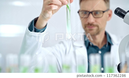 Scientist examining lab tube with a green fluid. Microbiology and science concept Scientist examining lab tube with a green fluid. Microbiology and science concept 117362286