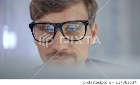 Businessman with glasses looking intently obscured partially by a translucent surface of laptop. Business concept Businessman with glasses looking intently obscured partially by a translucent surface of laptop. Business concept 117362534