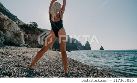 Woman in Black Bathing Suit Poses on a Pebble Beach 117363030