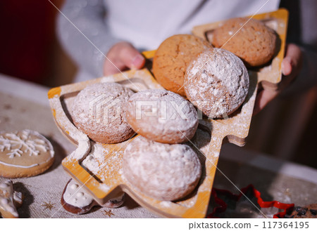 Hands hold cookies on a plate in the shape of a Christmas tree. 117364195