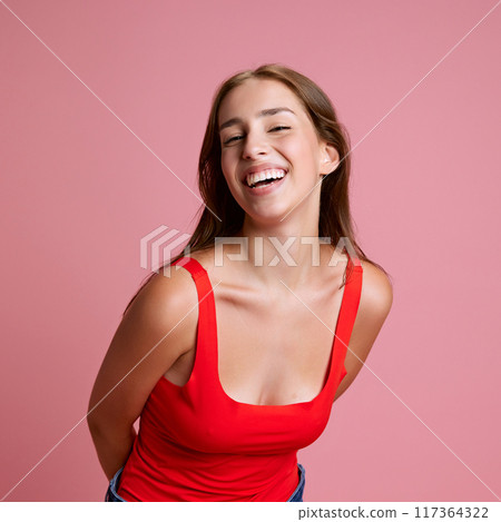 Portrait of beautiful young girl in red top cheerfully smiling, posing against pink studio background. Happiness, joy and fun Portrait of beautiful young girl in red top cheerfully smiling, posing against pink studio background. Happiness, joy and fun 117364322