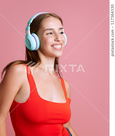 Portrait of beautiful, young, happy smiling girl listening to music in headphones against pink studio background 117364330