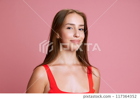 Portrait of beautiful young girl in red top posing with little tender smile against pink studio background Portrait of beautiful young girl in red top posing with little tender smile against pink studio background 117364352