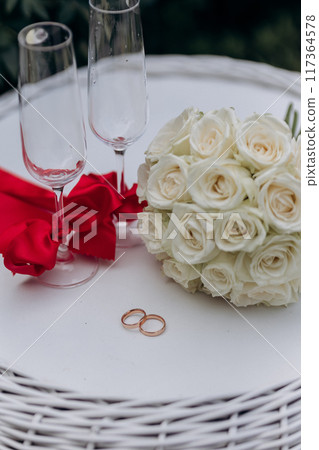 Elegant wedding setting with white roses, wedding rings, and champagne glasses, perfect for celebration 117364578