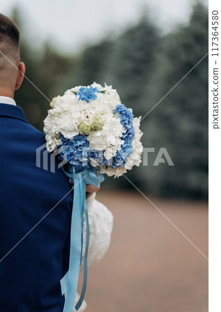 Groom holding a blue and white hydrangea wedding bouquet, symbolizing love and unity on special day 117364580