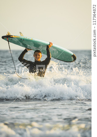 Happy young man lifting his surfboard above his head 117364872