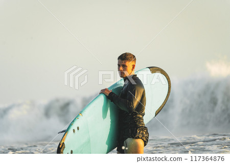 Young surfer in wetsuit looking focused with a wave behind him Young surfer in wetsuit looking focused with a wave behind him 117364876