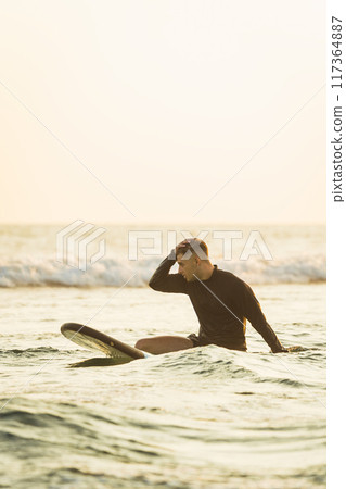 Surfer in the middle of the ocean with hand on head Surfer in the middle of the ocean with hand on head 117364887