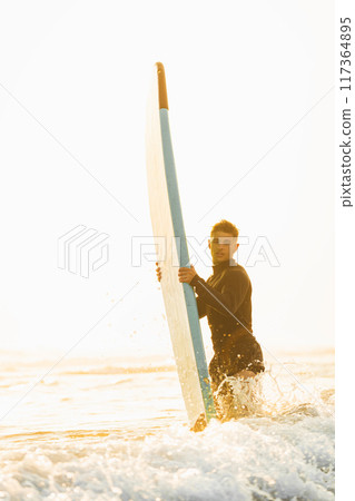 Surfer entering the water with his surfboard at sunrise Surfer entering the water with his surfboard at sunrise 117364895
