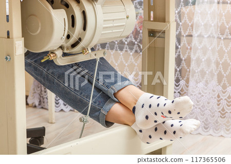 Female feet on the pedal of a sewing machine, motor Female feet on the pedal of a sewing machine, motor 117365506