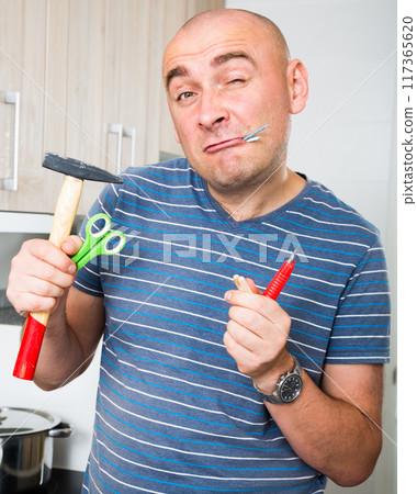 Imposing man in prime of life holds in teeth of screws and holding hammer Imposing man in prime of life holds in teeth of screws and holding hammer 117365620
