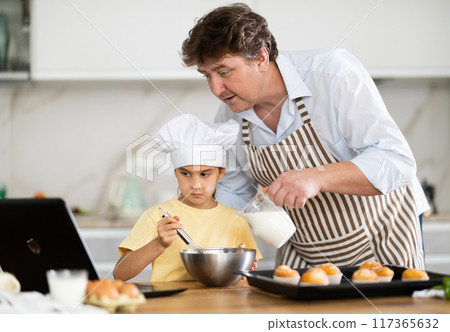 Father and little daughter prepare muffins according to a recipe from Internet Father and little daughter prepare muffins according to a recipe from Internet 117365632