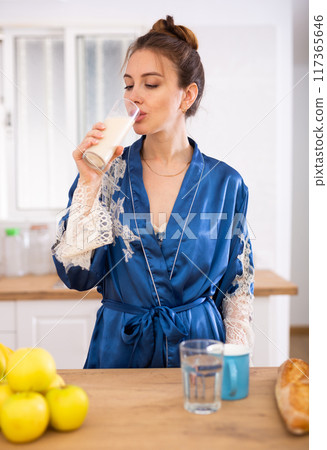 Woman in housecoat drinking protein shake for weight loss at breakfast in kitchen Woman in housecoat drinking protein shake for weight loss at breakfast in kitchen 117365646